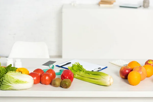 Pílulas, smartphone com tela em branco, área de transferência com caneta, frutas e legumes frescos na mesa — Fotografia de Stock