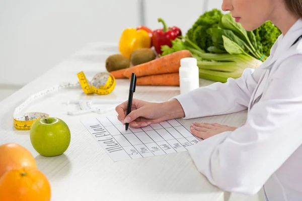 Visão cortada da escrita nutricionista no plano de refeições no local de trabalho — Fotografia de Stock