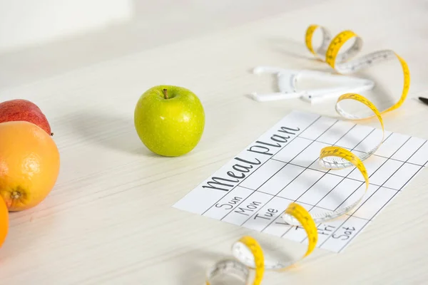 Plan de comidas, pinza, cinta métrica y frutas frescas en la mesa - foto de stock