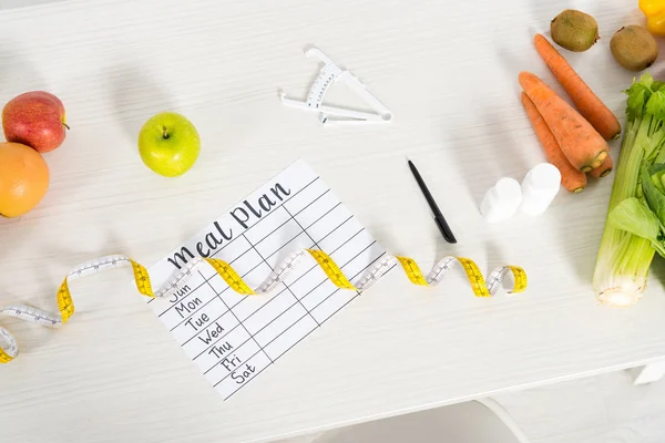 Top view of meal plan, measure tape, pen, caliper, pills and fresh fruits and vegetables on table — Stock Photo