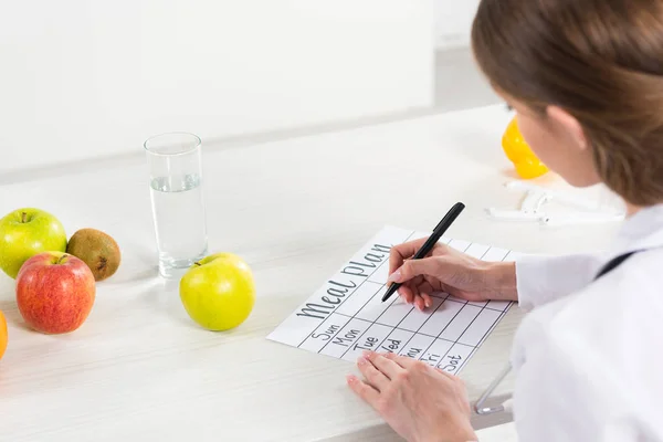 Vue recadrée de diététiste écrivant le plan de repas à table — Photo de stock