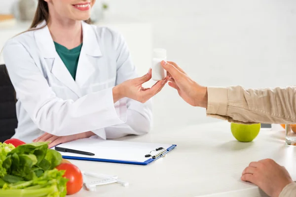 Vista recortada del dietista dando pastillas al paciente en el lugar de trabajo - foto de stock