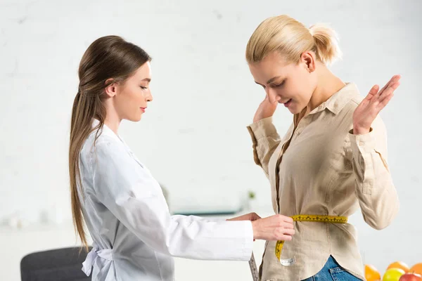 Side view of dietitian in white coat measuring waist for patient — Stock Photo