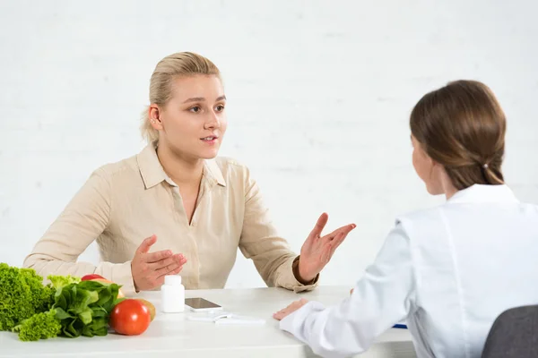 Patient and dietitian in white coat at table with fresh vegetables — Stock Photo