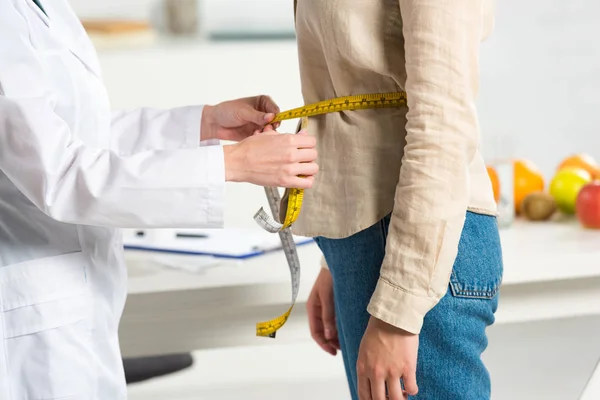 Vue recadrée de la diététiste en manteau blanc mesurant la taille pour le patient — Photo de stock