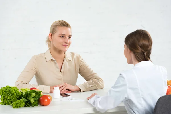 Ernährungsberaterin im weißen Kittel und Patientin schauen sich am Tisch an — Stockfoto