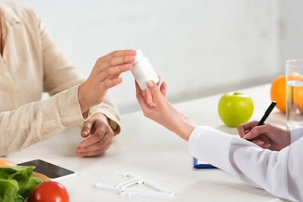 Vue recadrée de diététiste donnant des pilules pour le patient sur le lieu de travail — Photo de stock