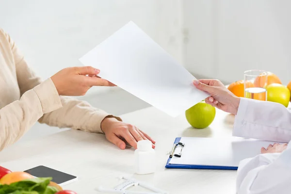 Visão cortada de nutricionista dando papel ao paciente no local de trabalho — Fotografia de Stock