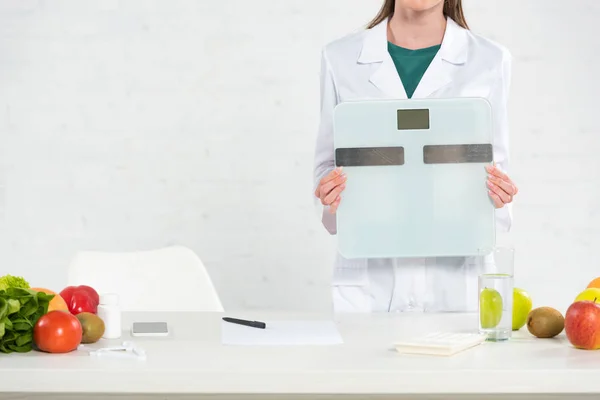 Ausgeschnittene Ansicht eines Ernährungswissenschaftlers im weißen Kittel, der digitale Waagen hält — Stockfoto
