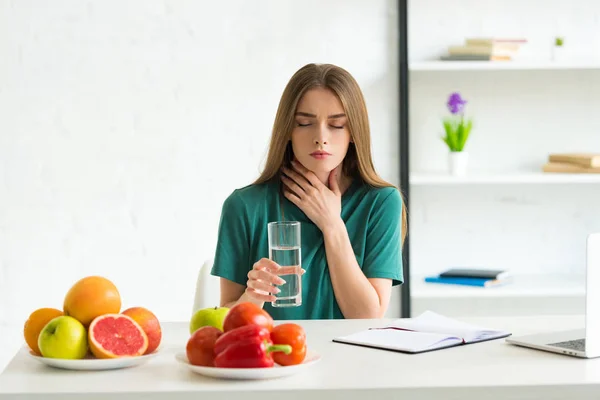 Vue de face de la femme avec les yeux fermés tenant un verre d'eau et touchant le cou — Photo de stock