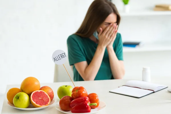 Femme avec masque médical éternuement assis à table avec des fruits, des légumes et des pilules — Photo de stock