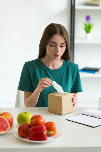 Fille allergique tenant des serviettes tout en étant assis à table avec des fruits et légumes — Photo de stock