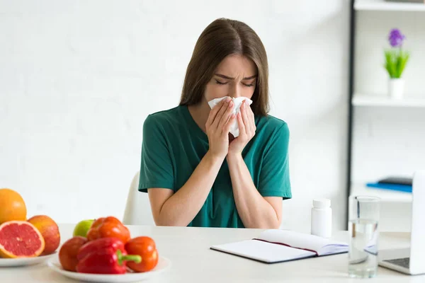 Donna che usa il tovagliolo mentre soffia il naso a tavola con frutta, verdura e pillole — Foto stock