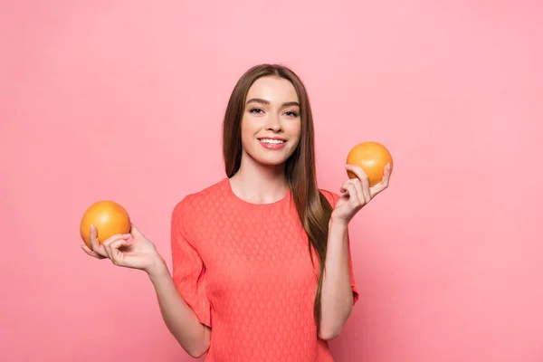 Vista frontale di attraente sorridente giovane donna che tiene pompelmi e guardando la fotocamera su rosa — Foto stock