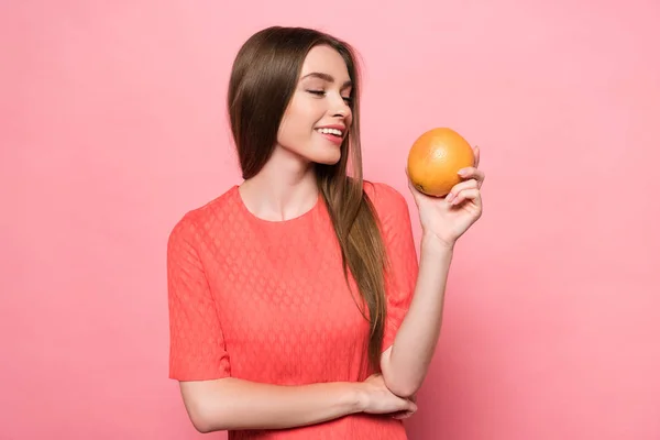 Привлекательная улыбающаяся молодая женщина держит грейпфрут на розовом — стоковое фото