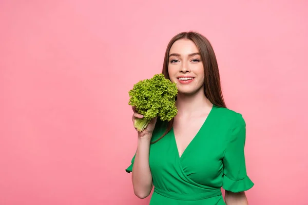 Attraktive lächelnde junge Frau mit Salat und Blick in die Kamera isoliert auf rosa — Stockfoto