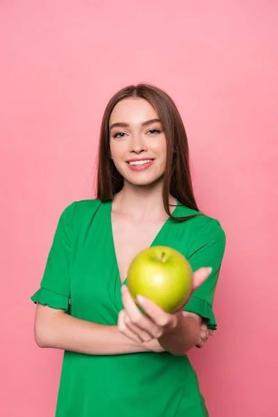 Вид спереду приваблива молода жінка тримає зелене яблуко і посміхається ізольовано на рожевому — стокове фото