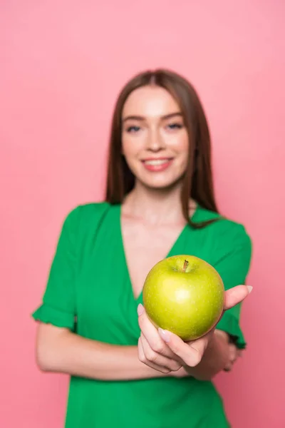 Enfoque selectivo de mujer joven atractiva sosteniendo manzana verde y sonriendo aislado en rosa - foto de stock