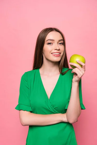 Attractive young woman holding green apple and smiling isolated on pink — Stock Photo