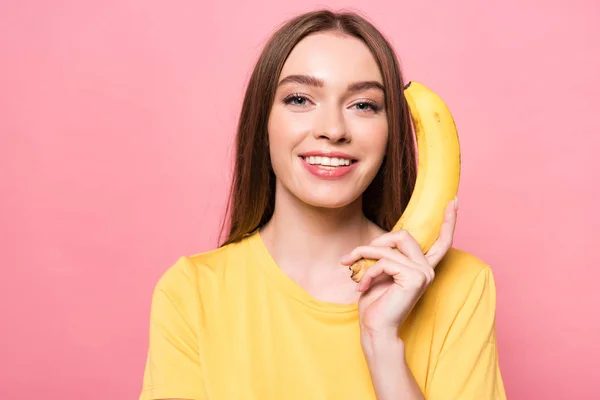 Menina sorridente atraente segurando banana e olhando para a câmera isolada em rosa — Fotografia de Stock