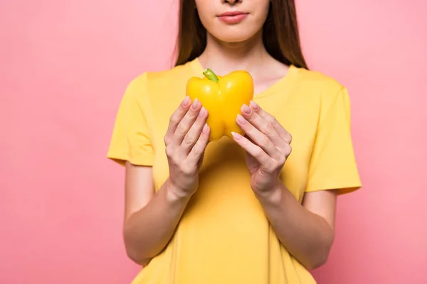 Cropped view of young woman in t-shirt holding yellow bell pepper on pink — Stock Photo