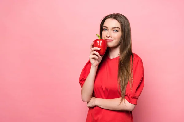 Lächelnde attraktive junge Frau mit rotem Paprika und Blick in die Kamera auf rosa — Stockfoto