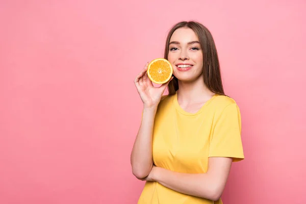Sorrindo menina atraente segurando cortado laranja e olhando para a câmera em rosa — Fotografia de Stock