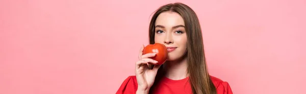 Scatto panoramico di giovane donna che tiene in mano il pomodoro e guarda la macchina fotografica isolata su rosa — Foto stock