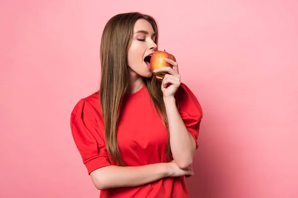 Приваблива молода жінка їсть яблуко з закритими очима на рожевому — стокове фото