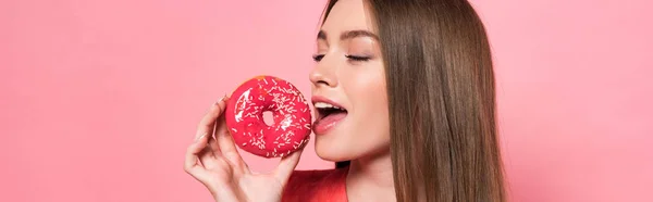 Panoramaaufnahme eines attraktiven Mädchens beim Donut essen mit geschlossenen Augen isoliert auf rosa — Stockfoto