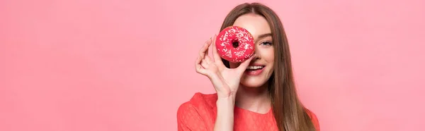 Panoramic shot of attractive smiling girl holding sweet doughnut isolated on pink — Stock Photo