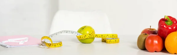 Panoramic shot of fresh fruits and vegetables, measure tape and textbook on table — Stock Photo