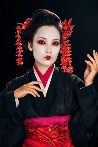 Geisha in black and red kimono and flowers in hair gesturing isolated on black — Stock Photo