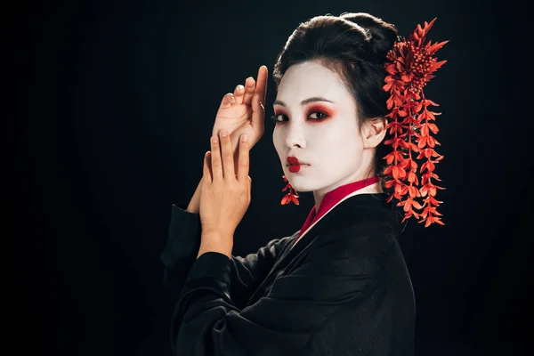 Vue latérale de la belle geisha en kimono noir et rouge et fleurs dans les cheveux isolés sur noir — Photo de stock