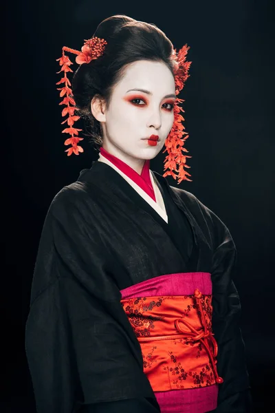 Gueixa em kimono preto e vermelho e flores em cabelo isolado em preto — Fotografia de Stock