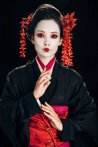 Bella geisha in kimono nero e rosso gesticolare isolata su nero — Foto stock