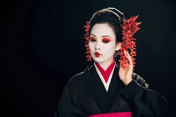 Bella geisha in kimono nero e rosso e fiori in capelli con mano vicino al viso isolato su nero con spazio copia — Foto stock