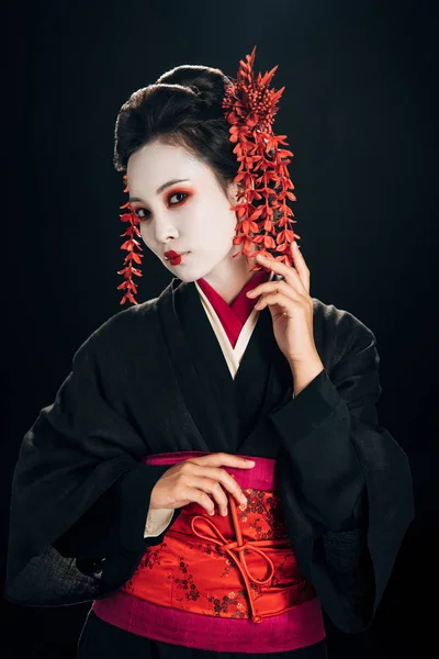 Beautiful geisha in black and red kimono and flowers in hair isolated on black — Stock Photo
