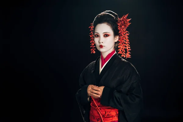 Calm beautiful geisha in black and red kimono and flowers in hair isolated on black — Stock Photo