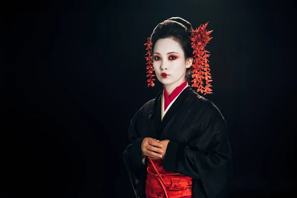 Calma hermosa geisha en negro y rojo kimono y flores en pelo aislado en negro - foto de stock