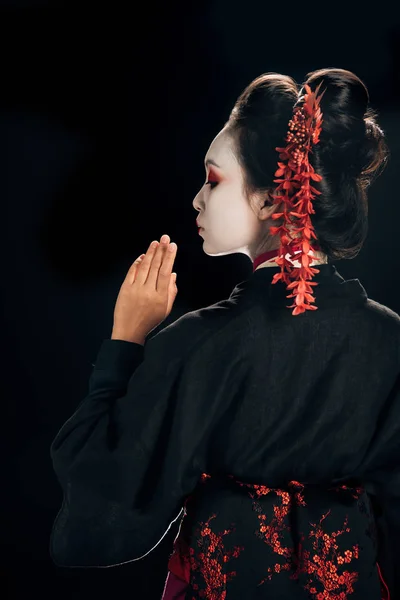 Вид на красивую гейшу в черно-красном кимоно и цветы в волосах, выделенных на черном — стоковое фото