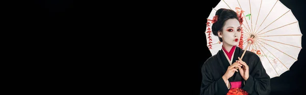 Bela gueixa no preto quimono com flores vermelhas no cabelo segurando tradicional asiático guarda-chuva isolado no preto com cópia espaço, tiro panorâmico — Fotografia de Stock