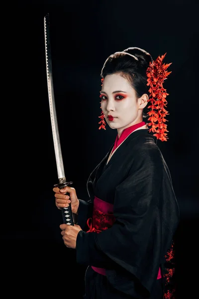 Geisha in black kimono with red flowers in hair holding katana isolated on black — Stock Photo