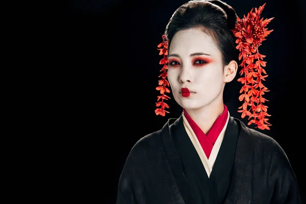 Ernste Geisha im schwarz-roten Kimono und Blumen im Haar isoliert auf schwarz — Stockfoto