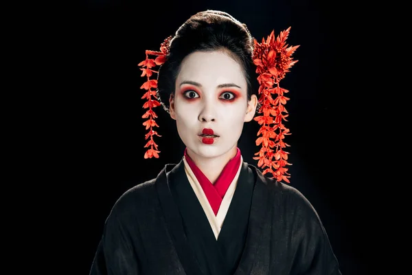 Impactado hermosa geisha en negro y rojo kimono y flores en pelo aislado en negro - foto de stock