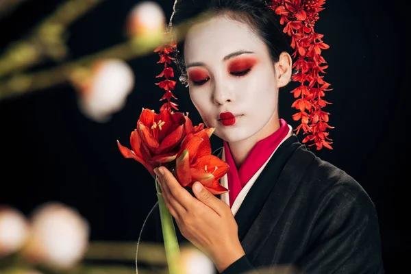 Selektiver Fokus der Geisha in schwarzem Kimono mit roten Blüten und Sakura-Zweigen isoliert auf schwarz — Stockfoto