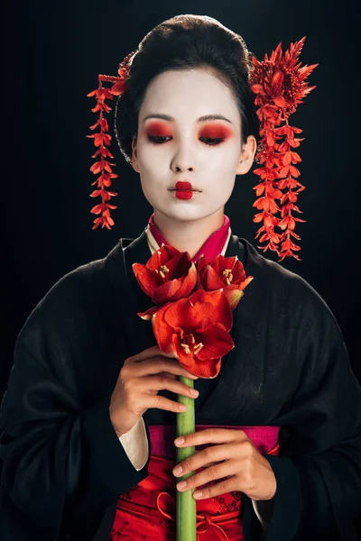 Junge Geisha im schwarzen Kimono mit roten Blüten isoliert auf schwarz — Stockfoto