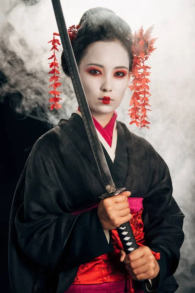 Confident beautiful geisha in black kimono holding katana in smoke — Stock Photo