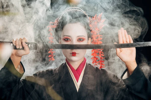 Foco seletivo da gueixa em quimono segurando katana em ramos de fumaça e sakura — Fotografia de Stock