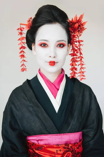 Smiling beautiful geisha in black kimono with red flowers in hair isolated on white — Stock Photo